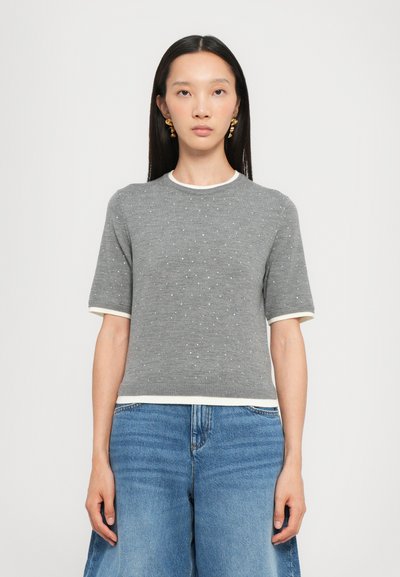 Maglietta corta in maglia grigia con texture a pois, colletto bianco e dettagli sul bordo, abbinata a un jeans blu a gamba larga.