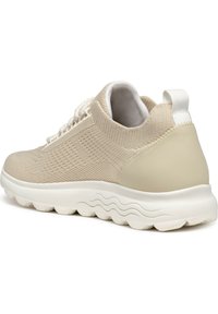 Scarpa sportiva beige con tomaia in maglia testurizzata e tallone liscio. Presenta una suola flessibile bianca con un motivo a onde e una chiusura con lacci.