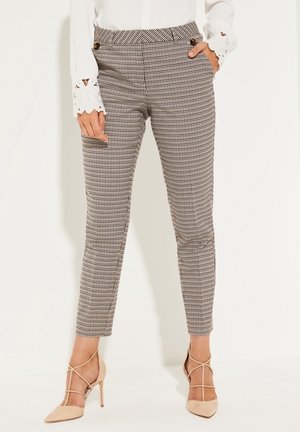Pantalons ajustés à carreaux en noir et blanc, dotés de poches, d'une coupe cintrée, et associés à des talons hauts nude.