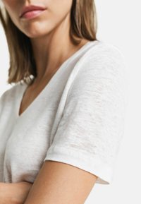 Weißes, leichtes V-Neck-T-Shirt mit kurzen Ärmeln, das eine sanfte Textur und ein dezentes, ungleichmäßiges Webdetail aufweist.