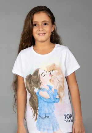 Mädchen mit langen braunen Haaren, das ein weißes T-Shirt trägt, auf dem eine Zeichnung eines Mädchens in Blau zu sehen ist, das einen kleinen flauschigen Hund hält.
