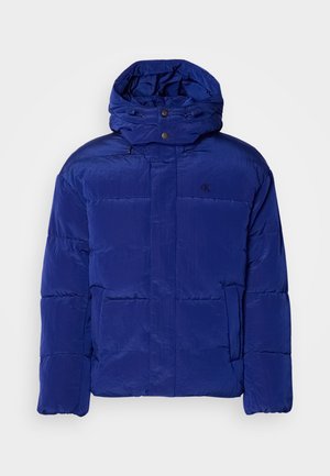 Blauwe pufferjack met een hoge kraag en verstelbare capuchon. Voorzien van een doorgestikte ontwerp en subtiele branding op de borst. Zacht, textuur materiaal.