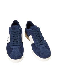Zapatillas de ante en azul marino con acentos blancos. Cuentan con una lengüeta acolchada y cordones planos. Suela de goma con un diseño robusto.