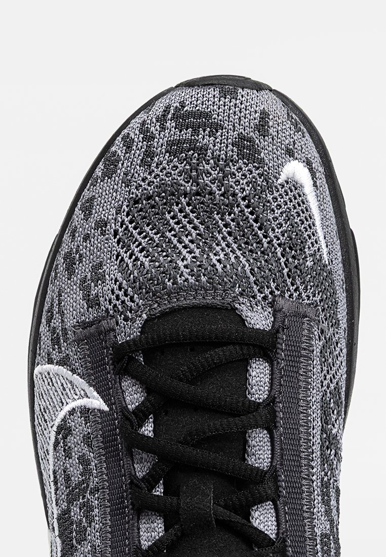 Zapatilla deportiva de Nike con parte superior de punto negro y gris, superficie texturizada, cierre de cordones y acento de logo blanco en el lateral. Suela de goma.