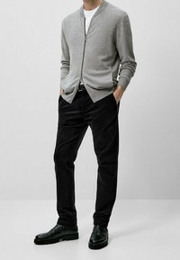 Szary sweter rozpinany na suwak z lekkiego materiału, zestawiony z czarnymi spodniami sztruksowymi i czarnymi skórzanymi butami. Prosty, czysty design.