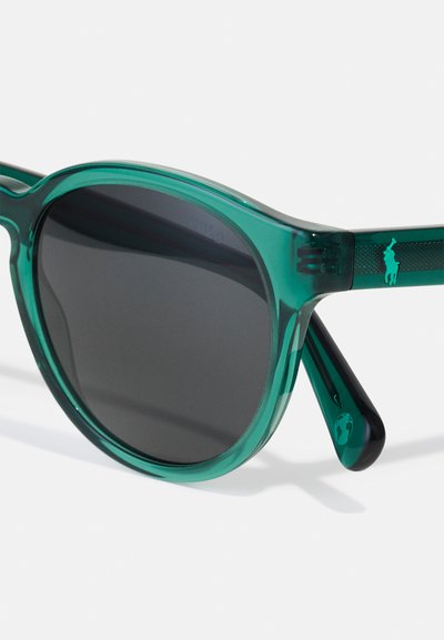 Óculos de sol de acetato verde transparente com lentes escuras. Forma redonda, hastes texturizadas e detalhe do logótipo numa das hastes.