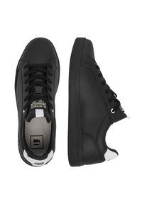 Melnas zemas sporta kurpes ar auklēm, baltu papēža cilpu un zīmola etiķeti uz mēles, redzamas no augšas un sāniem.