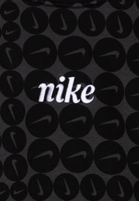 Černé tričko s celoplošným vzorem kruhových log; velké bílé vyšívané logo "nike" uprostřed; měkká textilní textura.