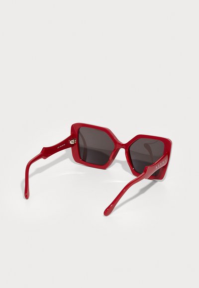 Sunglasses esagonali rossi con lenti scure, realizzati in plastica lucida. Presentano aste spesse con un logo discreto su un lato.