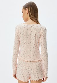 Ensemble de vêtements de détente rose clair avec des motifs floraux, texture côtelée et bords festonnés. Haut à manches longues et shorts en tissu doux et respirant.