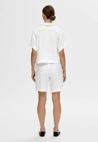 Hvid linned to-dels outfit bestående af en kortærmet, krave-top og matchende shorts, med en afslappet pasform og minimale designdetaljer.