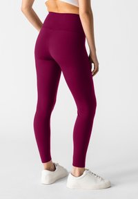 Bordeaux leggings gemaakt van rekbare stof, met een hoge tailleband. Gecombineerd met witte sneakers, die een slanke, aangesloten pasvorm tonen.