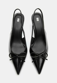 Čierne lakované slingback podpätky s špicatými špičkami, s dekoratívnou mašľou na prednej strane a hladkým povrchom na polstrovaných stielkach.