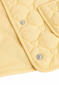 Tissu matelassé jaune avec couture en forme de cœur et deux boutons-pression argentés sur un coin plié.