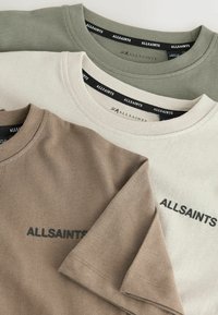 Tři trička v barvách khaki, krémové a hnědé. Každé má kulatý výstřih a vepředu se pyšní logem "ALLSAINTS" černým stehem.