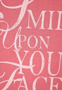 Roze t-shirt met grote, versleten witte tekst waarop staat "SMILE UPON YOUR FACE," met een zachte katoentextuur en casual ontwerp.