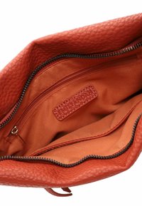 Red textured leather handbag interior with orange fabric lining, featuring a zippered pocket and a brand label embossed on the side.