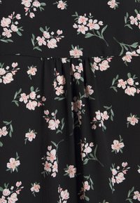 Tissu noir avec petits motifs floraux blancs et roses et feuilles vertes, avec un détail de couture plissée.