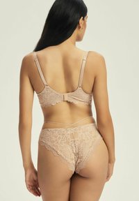 Koronkowy braletka i pasujące figi w miękkim beżu, z falbaniastymi brzegami, regulowanymi ramiączkami i krzyżującym się wzorem z tyłu.