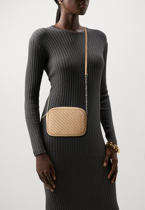 Sac en bandoulière tissé beige de forme rectangulaire, avec des bords en cuir et une chaîne, porté par-dessus une robe rayée noire.