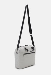 Graue Stoff-Schultertasche mit schwarzem Riemen, rechteckiger Form, oberen Griffen und einer vorderen Reißverschlusstasche. Glatte Textur und minimales Design.