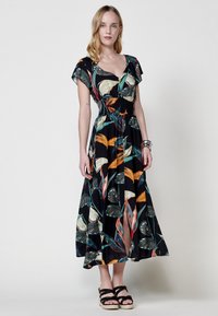 Vestido maxi negro con estampado floral que presenta vibrantes hojas en verde, naranja y amarillo; mangas cortas, cintura ajustada y falda con abertura.