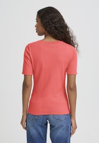 Pull en maille corail à manches courtes, col rond et silhouette ajustée. Le matériau semble doux avec une texture lisse.