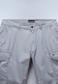 Hellgraue Cargohosen mit Front- und Seitentaschen, Knopfverschluss, Gürtelschlaufen und kleinem norwegischem Flaggen-Aufnäher an der linken Tasche.