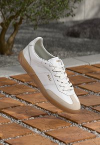 Sneakers din piele albă cu accente din suede bej, având vârful rotund, șireturi frontale și talpa din cauciuc bej, inscripționate cu numele brandului "BOSS."