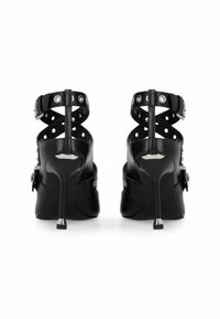 Chaussures noires à talons hauts avec un dos ouvert, dotées d'une bride chevauchante autour de la cheville, d'accentuations métalliques et d'un matériau en cuir texturé.