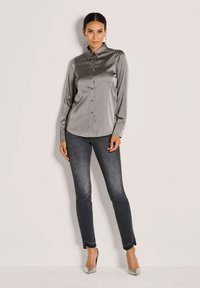 Silberne Satin-Hemd mit langen Ärmeln, kombiniert mit dunklen Slim-Fit-Jeans. Auffällige Creolen und hellfarbene Absatzschuhe vervollständigen den Look.