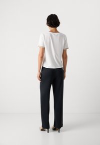 Top bianco a maniche corte con bordo testurizzato dorato, abbinato a pantaloni navy a gamba larga. Presenta una vestibilità comoda e un tessuto morbido.