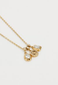 Collana in oro con tre pendenti: una goccia, un ciondolo rotondo decorativo e un ciondolo rettangolare, tutti adornati con pietre trasparenti.