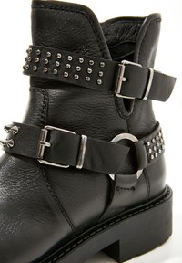 Bottine en cuir noir avec deux sangles cloutées, boucles argentées et semelle épaisse.