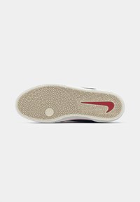 Apavu zole ar zīvju kaulu rakstu, bēšs gumija ar sarkano Nike svītru un baltu maliņu, skatīta no apakšas.