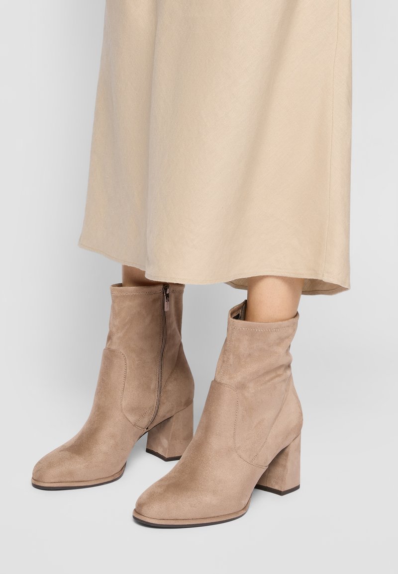 Beige suede ankle boots with a round toe, block heel, and side zipper, featuring a slouchy shaft design.