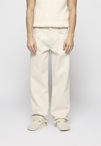 Beige weite Baumwollhosen mit einer glatten Textur und frontalen Taschen. Kombiniert mit einem gestrickten cremefarbenen Oberteil und beigen Holzclogs.