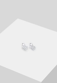 Sidabro gėlės formos auskarai su detalizuotais žiedlapiais, turintys poliruotą paviršių. Išdėstyti ant lygios baltos paviršiaus.