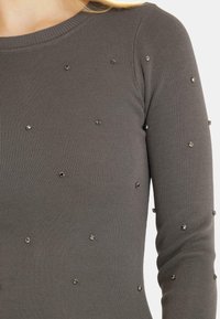 Top gris de manga larga con textura acanalada, que presenta adornos metálicos dispersos, resaltando un diseño ajustado.