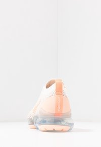 Scarpa da ginnastica leggera con tomaia in maglia color crema e accenti arancioni, dotata di suola trasparente con cuscinetto ad aria e linguetta per una facile calzata.