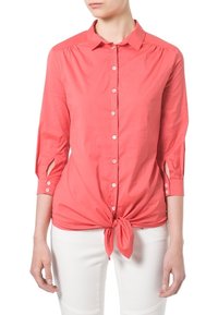 Camisa coral de botones con mangas largas y detalle de lazo en la parte delantera, con una textura suave y acentos de corte en los puños de las mangas.