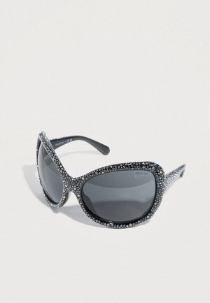 Occhiali da sole neri con una forma rotonda a occhio di gatto, caratterizzati da una montatura impreziosita da cristalli trasparenti e lenti scure.