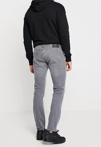 Grå denimjeans med slim fit, som har bakfickor och en svart logopatch. Bärs med en svart huvtröja och sneakers.