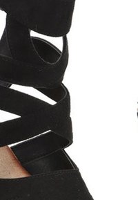 Zapatos de tacón alto de ante negro con múltiples tiras entrelazadas alrededor del tobillo y la puntera descubierta. La suela es de un color claro contrastante.