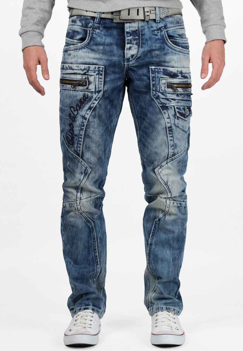Jeans in denim blu con finitura rovinata, dotati di numerose tasche con zip, dettagli ricamati e design a gamba dritta.