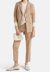 Krémový upravený blejzr se dvěma knoflíky, ladící zúžené kalhoty, krémový svetr a bílá kabelka se zlatým akcentem. Krémové mokasíny dokončují vzhled.