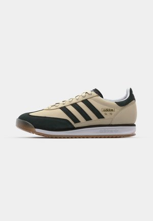 Sneaker bege com detalhes em verde escuro, três riscas pretas e uma língua em malha texturizada. Apresenta uma sola de borracha goma e a marca "adidas SL '72".