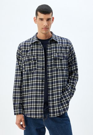 Marineblå og hvid ternet flannel skjorte med lange ærmer, knappet front, to brystlommer og en klassisk krave. Båret over en mørk top.
