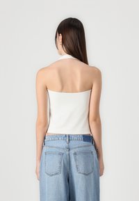 White halter neck top with a fitted design, paired with light blue high-waisted jeans featuring large pockets and a loose fit.