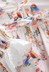 Sukienka w kwiaty wykonana z jasnoróżowej tkaniny, z wesołymi wzorami zwierząt i kwiatów, elastycznym paskiem w talii oraz białymi ażurowymi zdobieniami na rękawach.